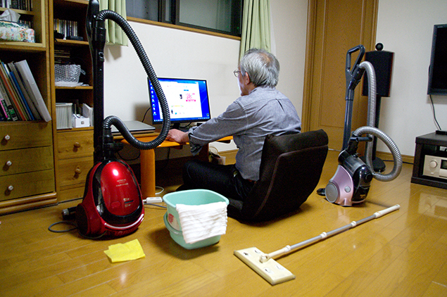 掃除機、バケツ、雑巾を手元に置いてパソコンをしている写真