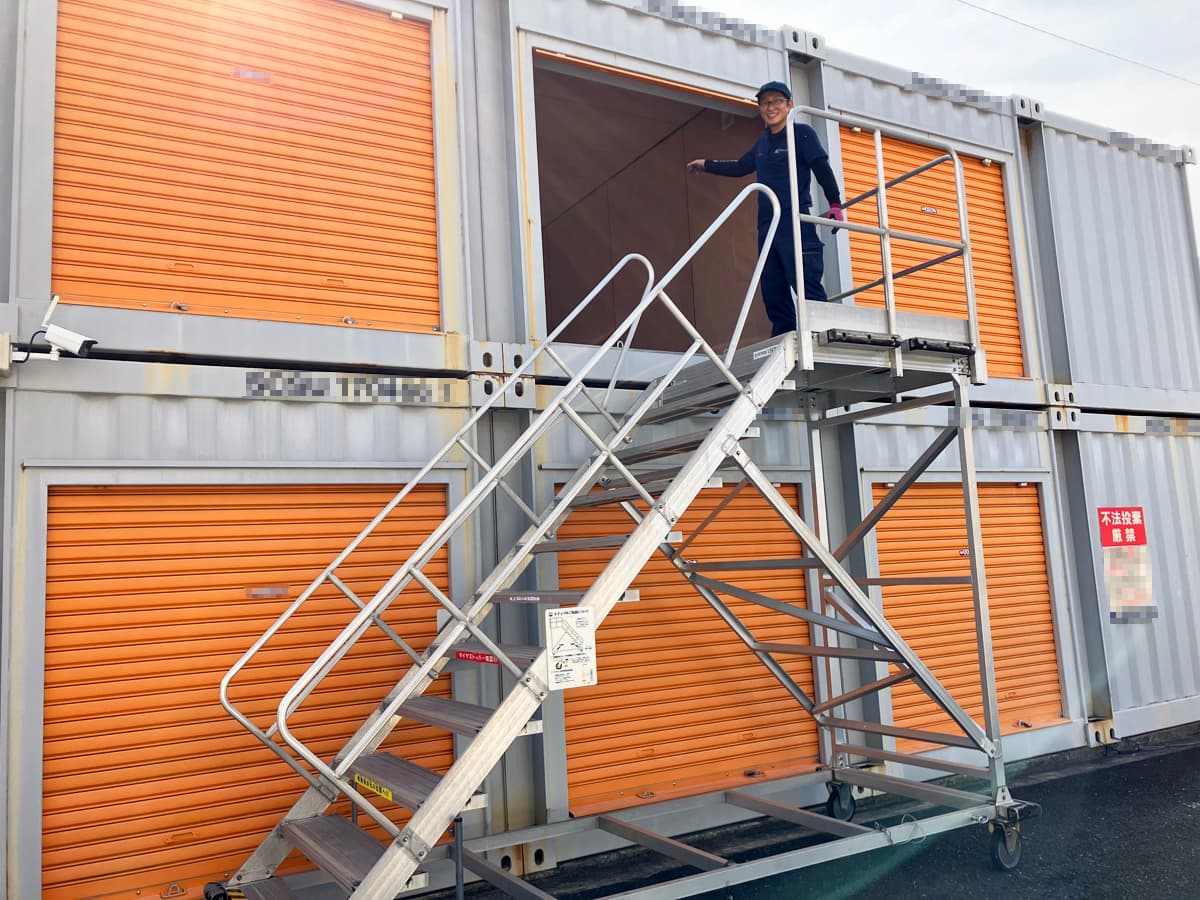 2階建てのレンタル倉庫前で移動式階段に上ったスタッフの写真