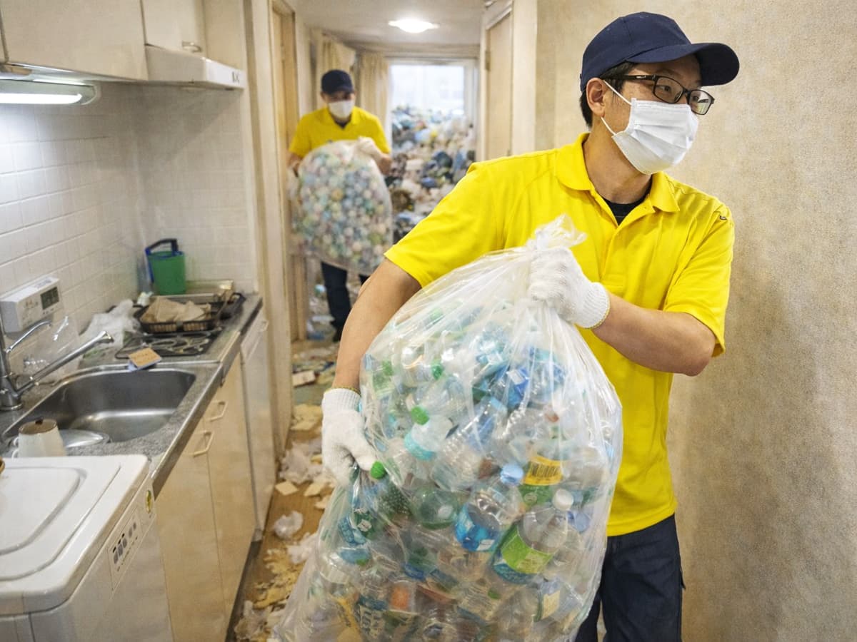 1Rのゴミ屋敷片付けの作業中、キッチンと廊下が一体になった通路で、袋に詰めたペットボトルを搬出している様子