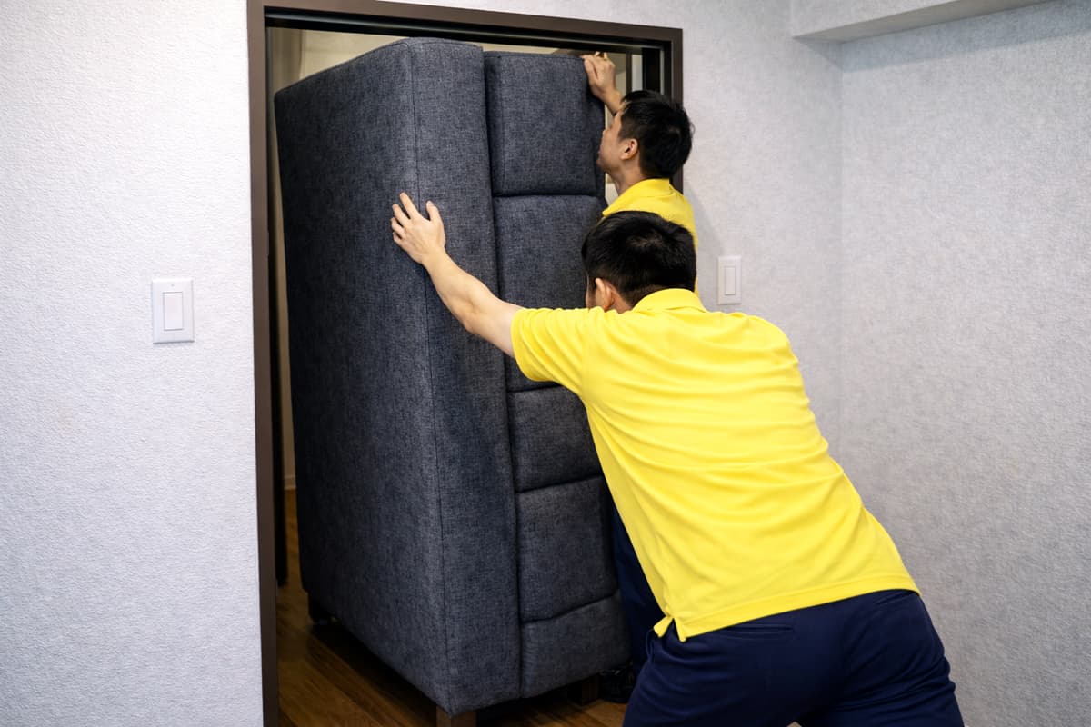 ドア枠ギリギリの幅で立てたソファを2人で慎重に搬出する作業スタッフの様子