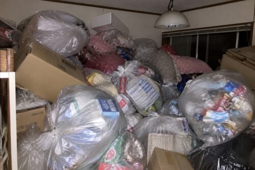 退去前のごみ屋敷状態の部屋に、袋詰めされたごみやダンボールが天井近くまで積み上がっている様子