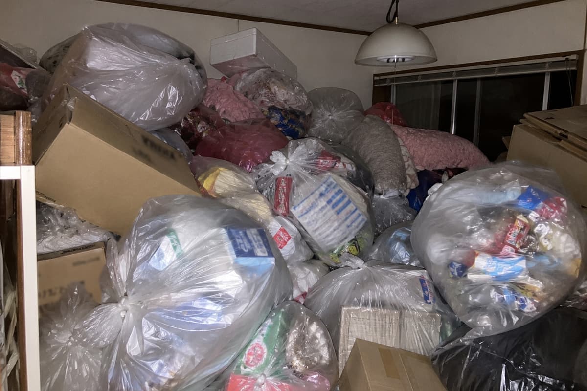 退去前のごみ屋敷状態の部屋に、袋詰めされたごみやダンボールが天井近くまで積み上がっている様子