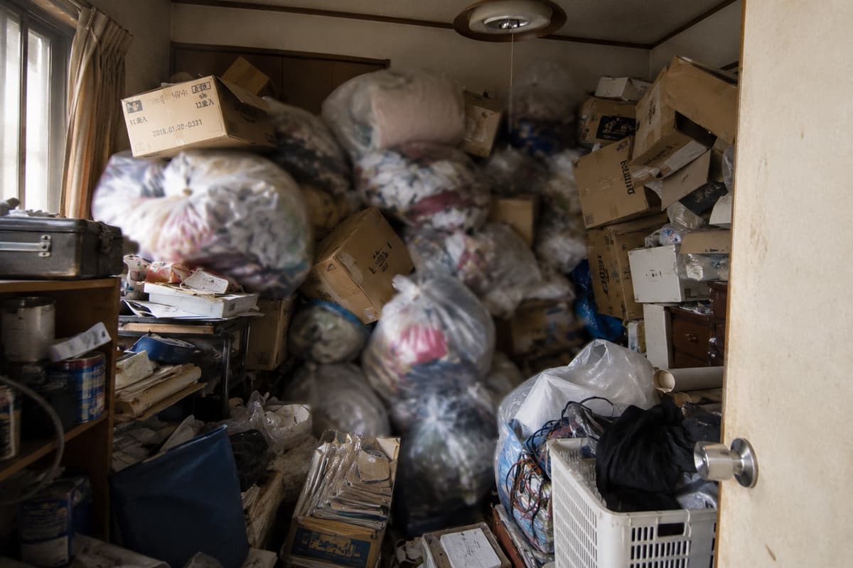 ごみ袋やダンボール、生活用品が部屋いっぱいに積み重なり、奥の様子が確認しにくい退去前の室内