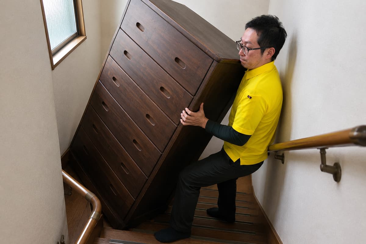 狭い階段で大型タンスを一人で運ぼうとするスタッフの危険な様子