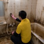 壁一面にカビや汚れが広がった浴室を清掃するスタッフ
