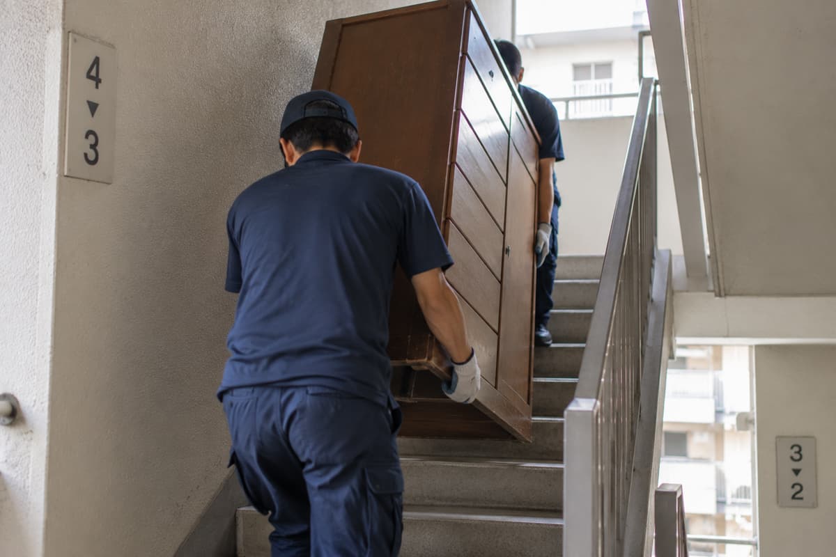 エレベーターのない団地の階段で大型家具を運び出す作業員