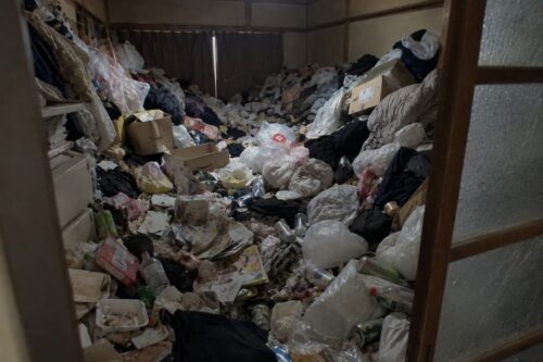 大量の衣類やごみ袋、段ボール、空き缶などで床一面が埋め尽くされた和室の片付け前の様子